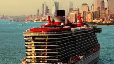 A large cruise ship sails past a city skyline - Brilliant Lady, Virgin Voyages