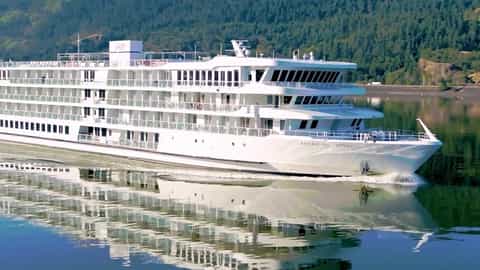 A white cruise ship sails on a calm river - American Heritage, American Cruise Lines