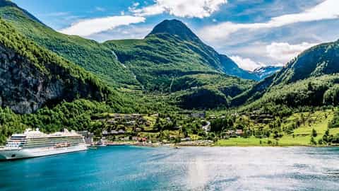 A large cruise ship sails in a blue fjord near a green mountain village - Viking Astrea, Viking Cruises