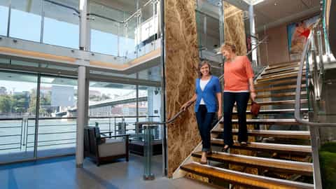 Two women descend a modern staircase inside a ship - Viking Embla, Viking River Cruises