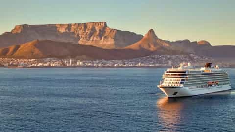 A cruise ship sails past a coastal city and mountains - Viking Lyra, Viking Cruises