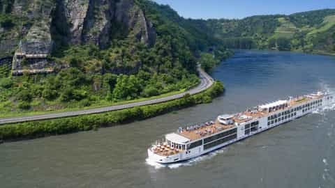 A river ship cruises past a scenic, tree-lined riverbank - Viking Magni, Viking River Cruises