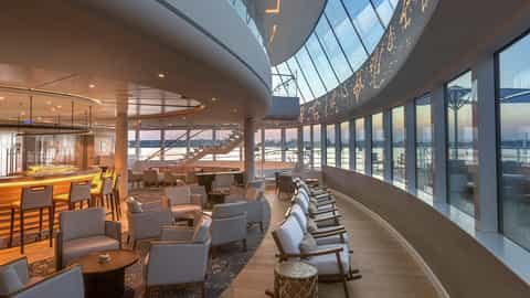 A modern lounge bar with large windows overlooking the water at sunset - Viking Mississippi, Viking River Cruises