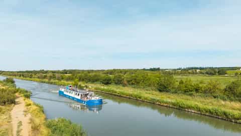 A blue and white river boat travels down a canal - Anne Marie barge, CroisiEurope