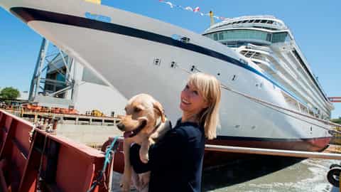 Woman holds a dog in front of a large ship - Viking Sea, Viking Cruises
