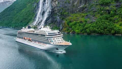 A cruise ship sails past a waterfall in a green fjord - Viking Sky, Viking Cruises