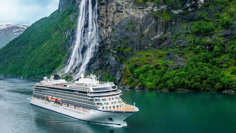 A cruise ship sails past a waterfall in a green fjord - Viking Sky, Viking Cruises