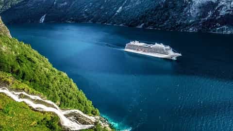 A cruise ship sails through a fjord near a waterfall - Viking Venus, Viking Cruises