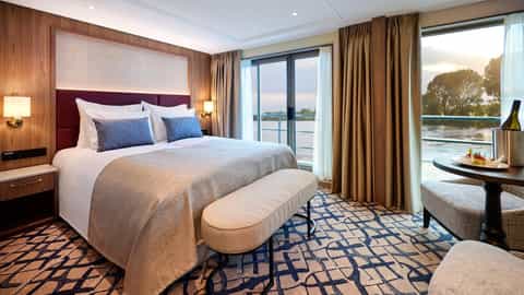 A suite bedroom with a balcony overlooking a river at sunset - VIVA Ruby, Viva Cruises