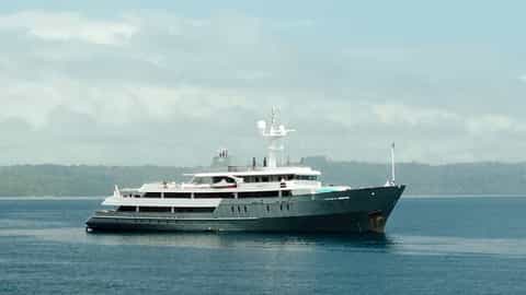 A woman paddles on a board near a large yacht - Aqua Blu, Ponant Cruises