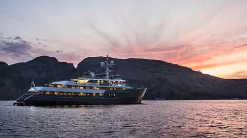A yacht sails on the water at sunset near mountains - Aqua Blu, Ponant Cruises