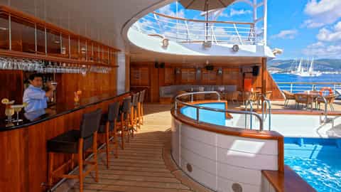A bartender makes drinks at a bar next to a pool - Wind Spirit, Windstar Cruises