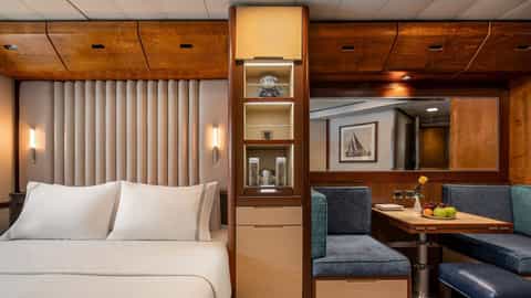 A suite interior with a bed, seating area, and table - Wind Spirit, Windstar Cruises