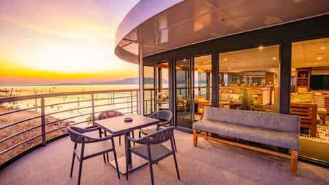 A balcony with a table, chairs, and a bench overlooks a sunset - Zimbabwean Dream, CroisiEurope