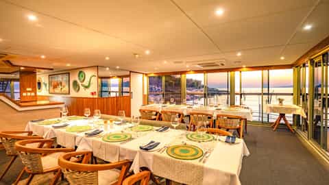 A dining room with tables set for dinner overlooking a sunset - Zimbabwean Dream, CroisiEurope