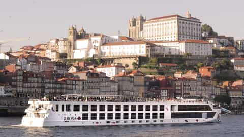 A river ship sails past a historic European city - Arosa Alva, A Rosa Cruises