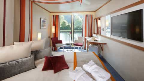 A river view suite with a bed, seating area, and desk - Arosa Donna, A Rosa Cruises