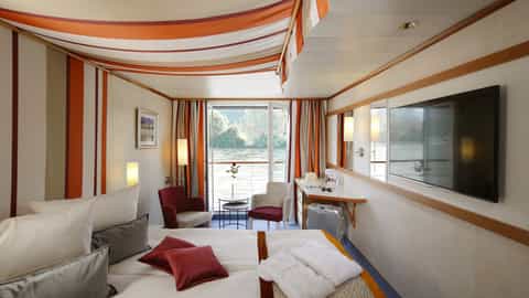A river view suite with a bed, seating area, and balcony - Arosa Donna, A Rosa Cruises