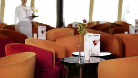 A lounge with orange and red seating and a flower - Arosa Donna, A Rosa Cruises