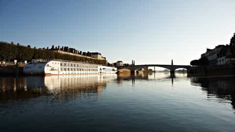 A river ship is docked beside a city and bridge - Arosa Luna, A Rosa Cruises