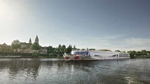 A river ship sails past a European town on a sunny day - Arosa Stella, A Rosa Cruises