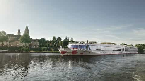 A river ship passes a European town on a sunny day - Arosa Stella, A Rosa Cruises