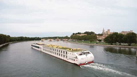 A river cruise ship sails past a historic city and bridge - Arosa Stella, A Rosa Cruises