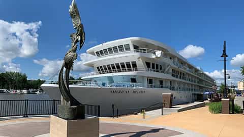 A white cruise ship is docked beside a waterfront promenade - ACL American Melody, American Cruise Lines