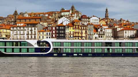 A river ship sails past a colorful city on a hill - Avalon Alegria, Avalon Waterways