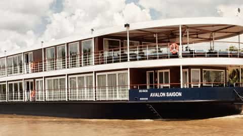 A river ship sails on a muddy river past palm trees - Avalon Saigon, Avalon Waterways