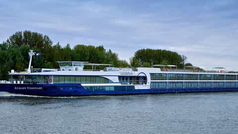 A blue and white river ship cruises on a wide waterway - Avalon Visionary, Avalon Waterways