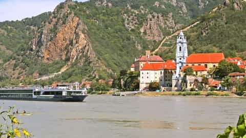 A river ship sails past a historic village - Avalon Vista, Avalon Waterways