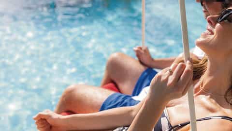 A couple relaxes by a sunlit pool - Celebrity Ascent, Celebrity Cruises