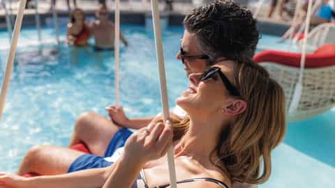 A couple relaxes on a swing by the pool - Celebrity Eclipse, Celebrity Cruises
