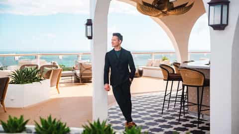 A man in a suit poses on a ship's deck by a bar - Celebrity Edge, Celebrity Cruises