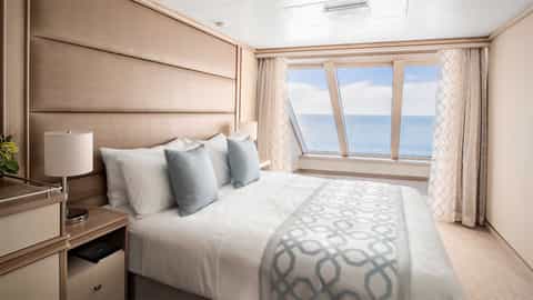 A well-made bed faces a large window with ocean views - Discovery Princess, Princess Cruises