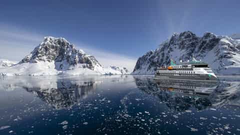 A ship sails through a bay with snow-covered mountains - Douglas Mawson, Aurora Expeditions