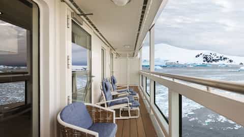A balcony with chairs overlooks an icy sea and snowy mountains - Douglas Mawson, Aurora Expeditions