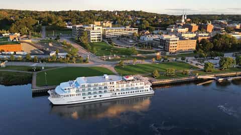A river ship is docked next to a city on a sunny day - ACL American Constellation, American Cruise Lines