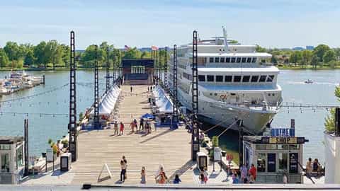 A ship is docked next to a pier with market stalls - ACL American Constellation, American Cruise Lines