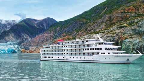A white cruise ship sails past a glacier and mountains - ACL American Constellation, American Cruise Lines