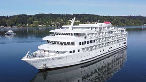 A white cruise ship sails on calm blue water - ACL American Constellation, American Cruise Lines