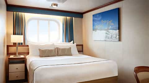 A stateroom bed with a large oval window - Emerald Princess, Princess Cruises