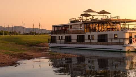 A river boat is docked on a calm river at sunset - African Dream, CroisiEurope