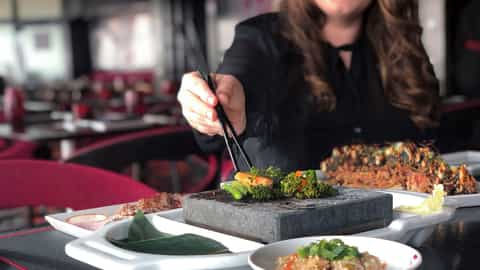 A woman uses chopsticks to cook vegetables on a hot stone - Explorer Of The Seas, Royal Caribbean
