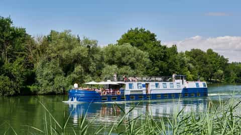 A blue and white riverboat cruises on a calm waterway - Jeanine barge, CroisiEurope