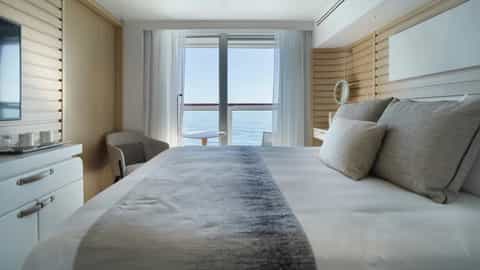 A modern cruise ship suite bedroom with a balcony view - Le Bellot, Ponant Cruises