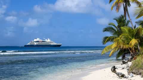 A cruise ship sails on the ocean near a tropical beach - Le Boreal, Ponant Cruises