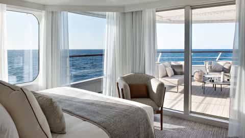 A suite with a bed, chair, and balcony overlooking the ocean - Le Bougainville, Ponant Cruises