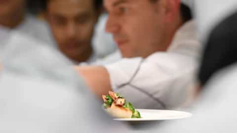 Chefs in uniform prepare a plated dish in a kitchen - Le Champlain, Ponant Cruises